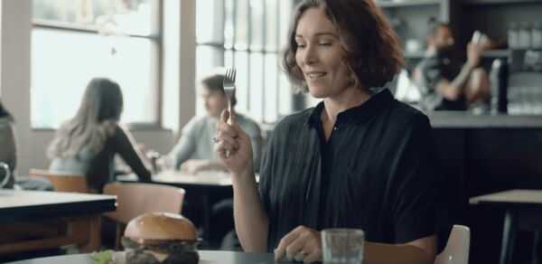 A woman sitting at a table, enjoying a burger